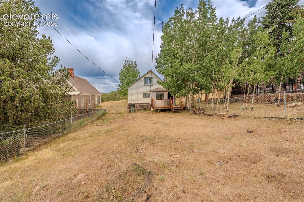 Image 34 of 40: Expansive sloped property featuring a chain-link fence, mature trees, and n