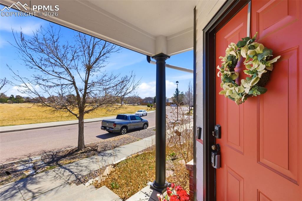 Image 3 of 44: Covered front porch with a paneled coral entry door and black porch column