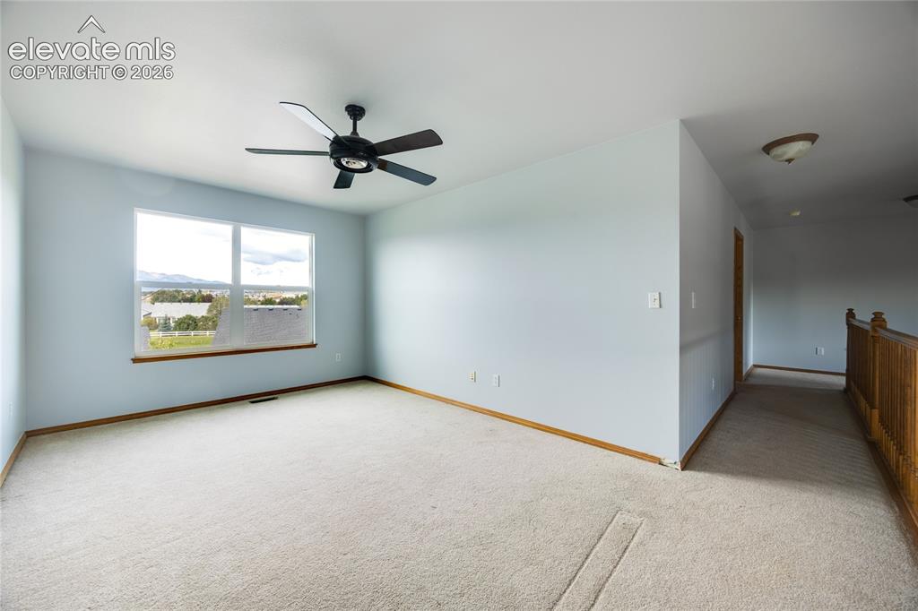 Image 14 of 34: Carpeted room with a ceiling fan, a large window, and a wooden railing