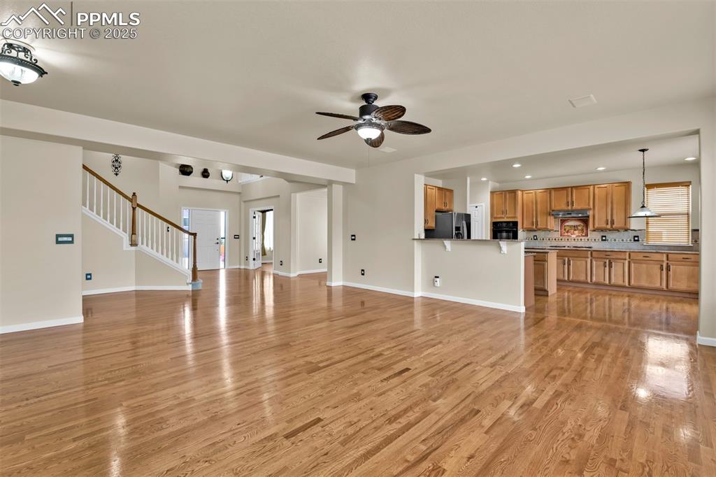 Image 10 of 50: Unfurnished living room with a ceiling fan, light wood-type flooring, stair