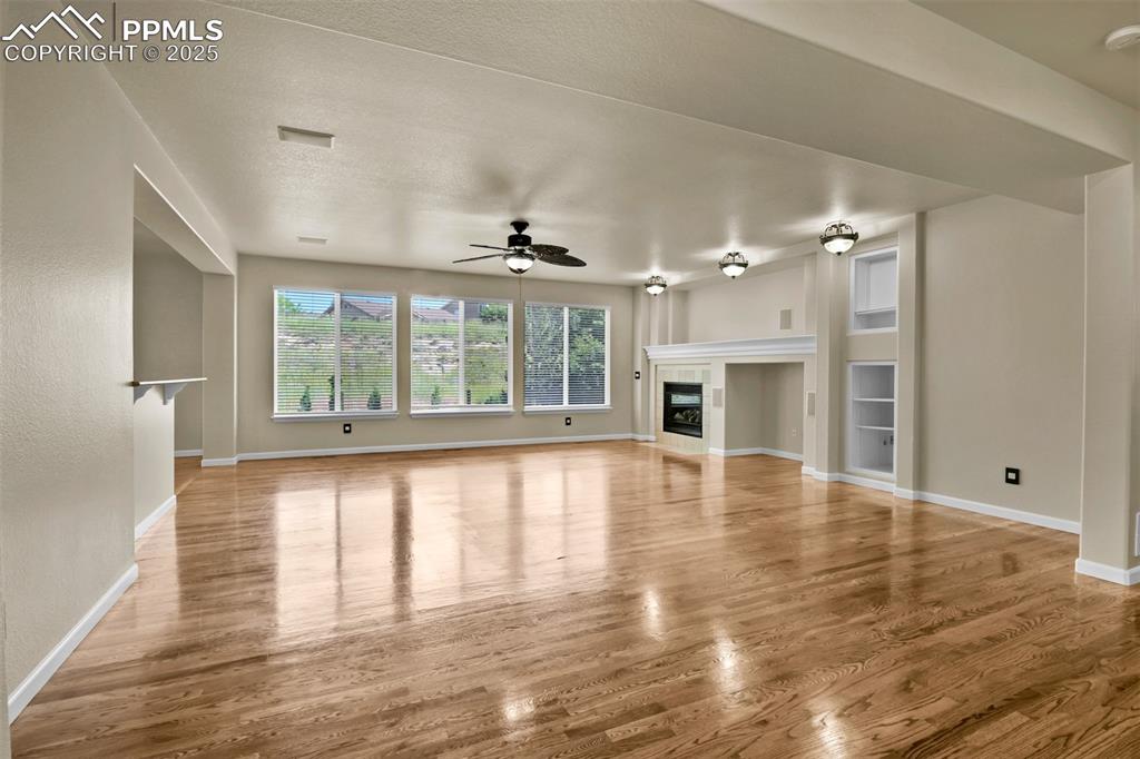 Image 20 of 50: Unfurnished living room with ceiling fan, wood finished floors, and a tiled