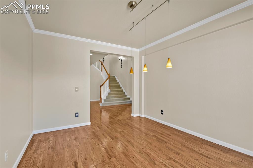 Image 24 of 50: Unfurnished room with light wood-style floors, stairs, and crown molding