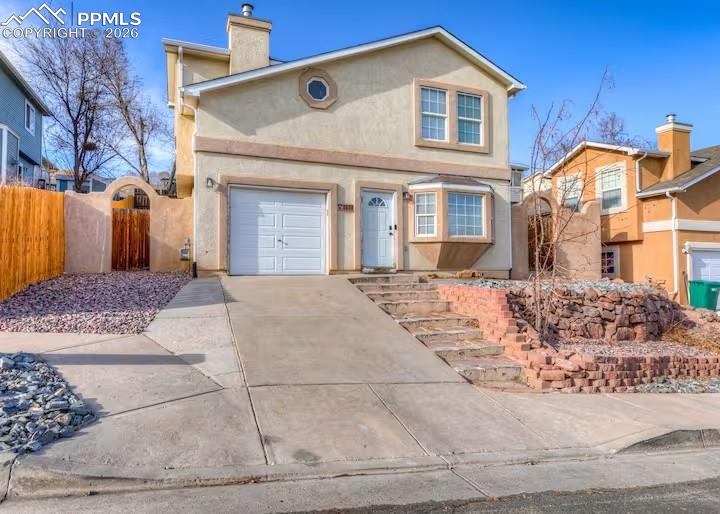 Image 1 of 10: View of front of home with stucco siding, a chimney, concrete driveway, and