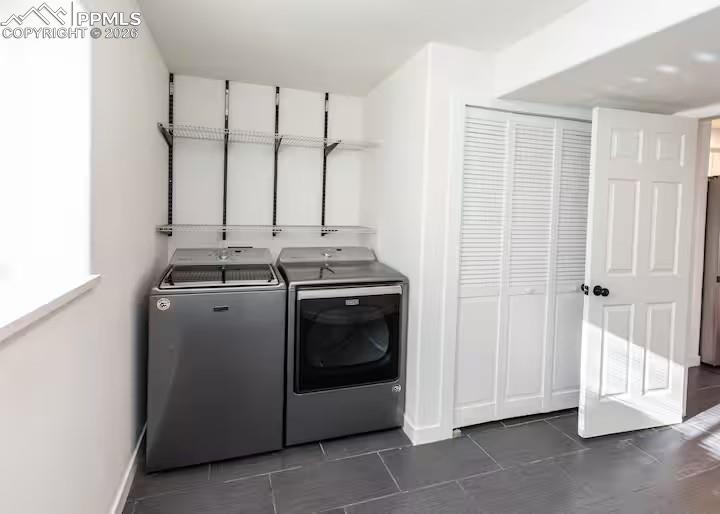 Image 19 of 23: Laundry area with dark tile patterned floors and washing machine and clothe