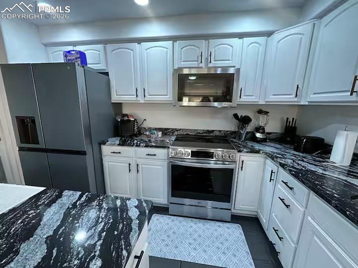 Image 8 of 10: Kitchen with stainless steel appliances, dark stone countertops, and white 