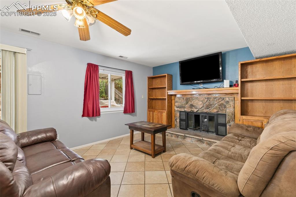 Image 20 of 36: Living room with light tile patterned floors, a fireplace, and a ceiling fa