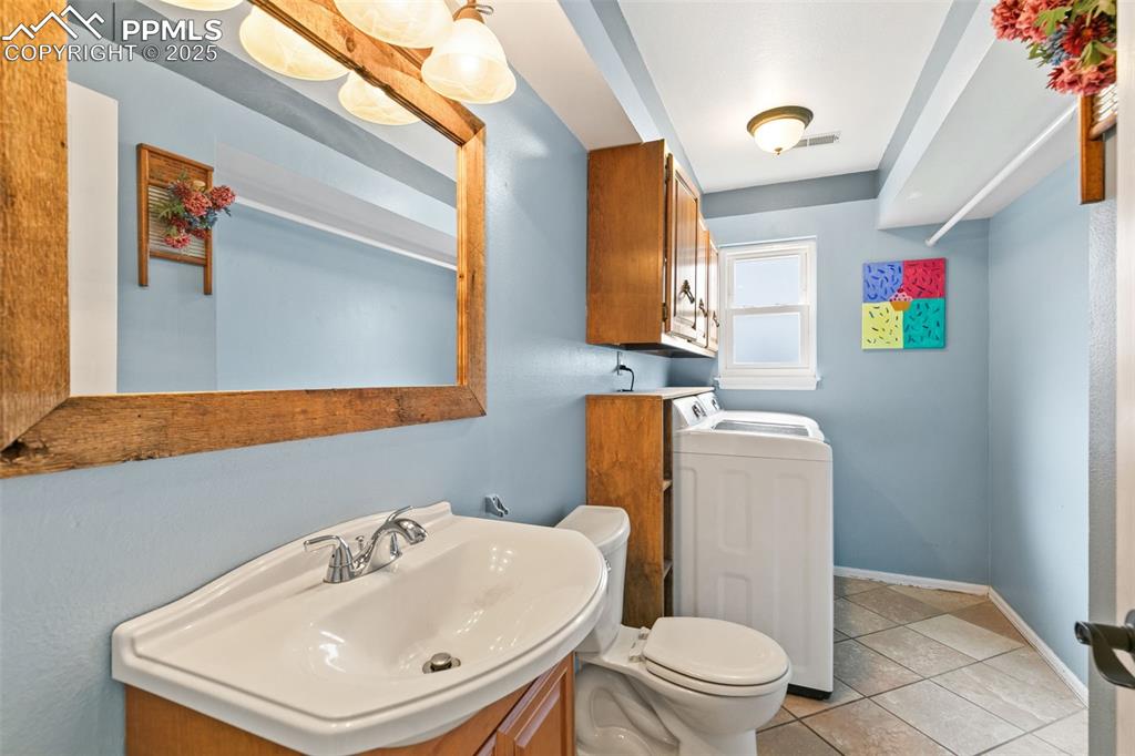 Image 21 of 36: Half bathroom with light tile patterned floors, vanity, and washer and clot
