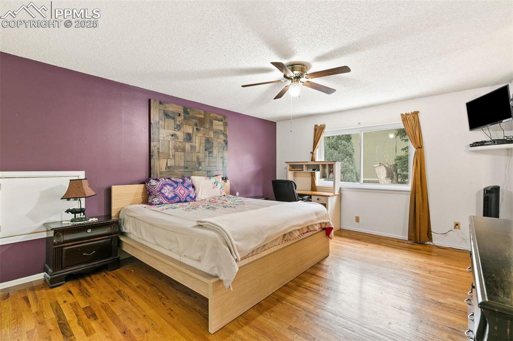 Image 22 of 36: Bedroom featuring light wood-type flooring, ceiling fan, and a textured cei