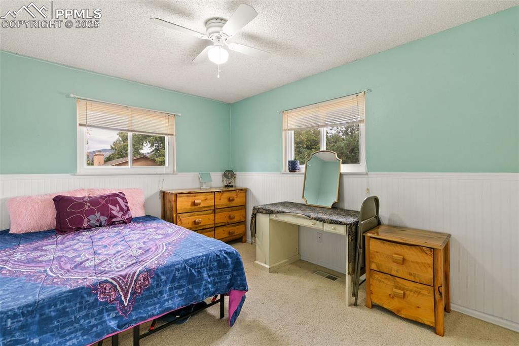 Image 25 of 36: Bedroom with a wainscoted wall, light colored carpet, a ceiling fan, and a 