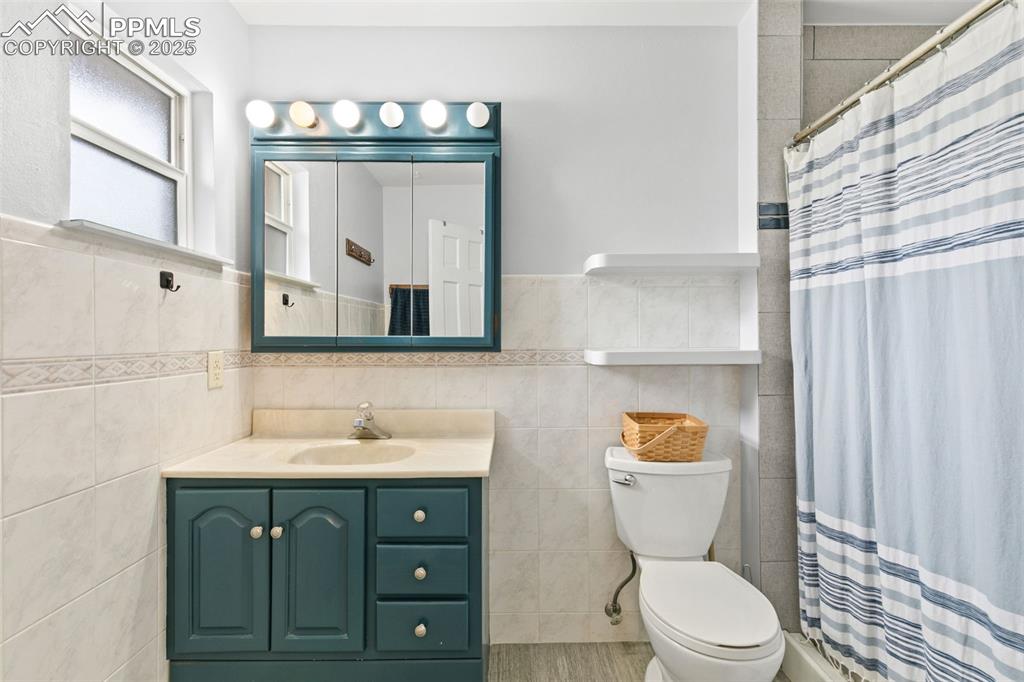 Image 27 of 36: Bathroom featuring tile walls, vanity, a stall shower, and wainscoting