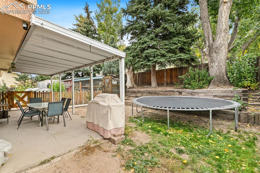 Image 34 of 36: Fenced backyard with a trampoline, a patio, and outdoor dining area