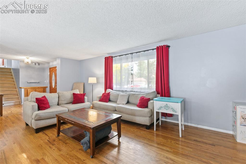 Image 6 of 36: Living area with stairs, a textured ceiling, and light wood finished floors