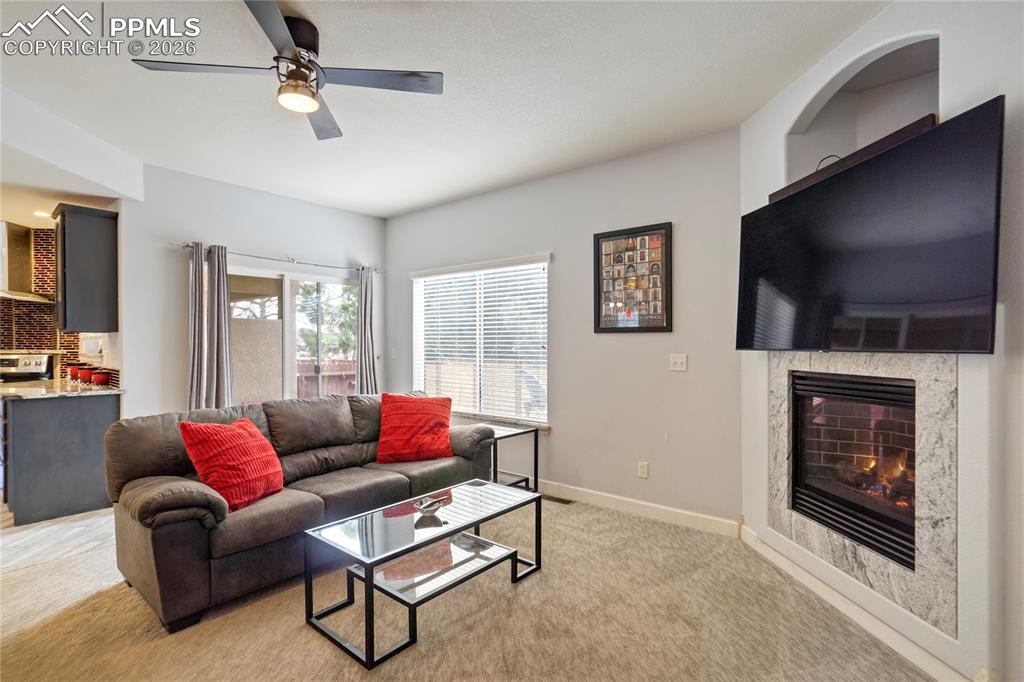 Image 7 of 42: Living area featuring ceiling fan, a tile fireplace, and light colored carp