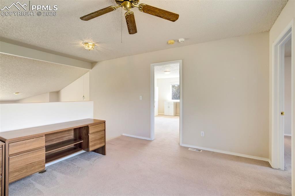 Image 28 of 44: Carpeted loft space featuring a built-in wood-finish desk, ceiling fan, and