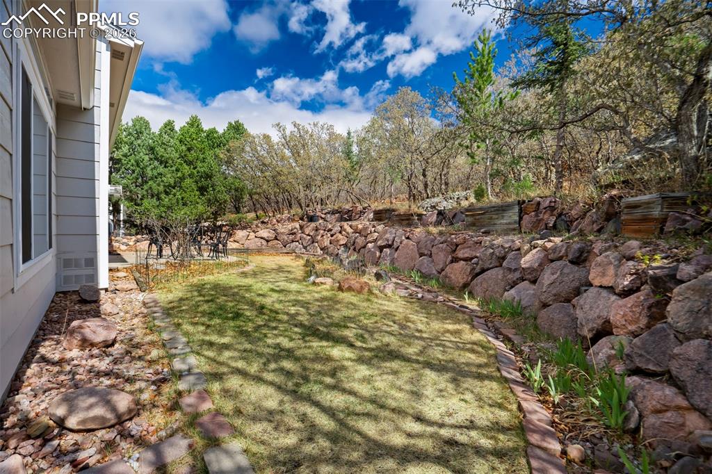 Image 35 of 44: Terraced outdoor space featuring a stone retaining wall, mature trees, mani