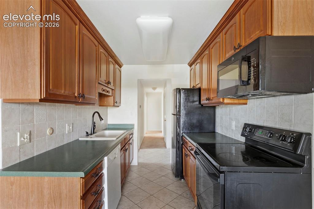 Image 10 of 18: Galley kitchen featuring wood-finish cabinetry, black appliances, a white t