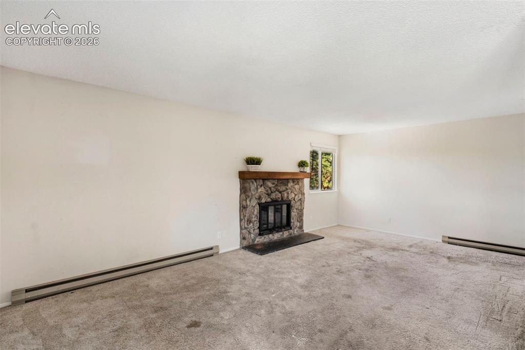 Image 6 of 18: Stone-surround fireplace with a wood mantle, carpet flooring, and a single 
