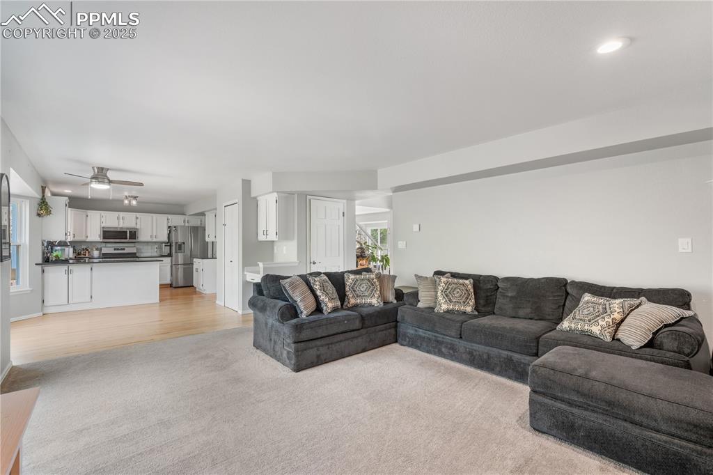 Image 13 of 50: Living room with light wood-style floors, a ceiling fan, light carpet, and