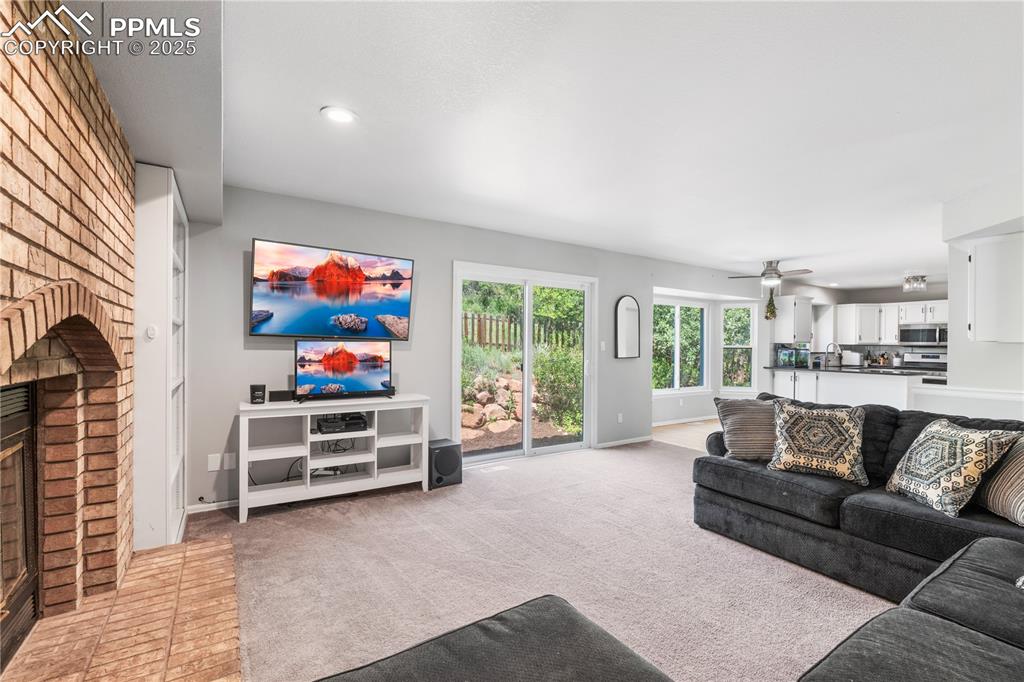 Image 14 of 50: Living room featuring a brick fireplace, light colored carpet, ceiling fan,