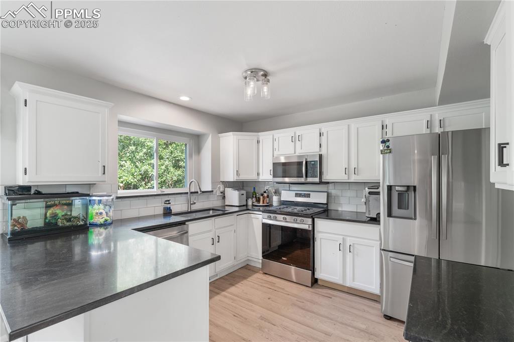 Image 18 of 50: Kitchen with stainless steel appliances, dark countertops, white cabinetry,