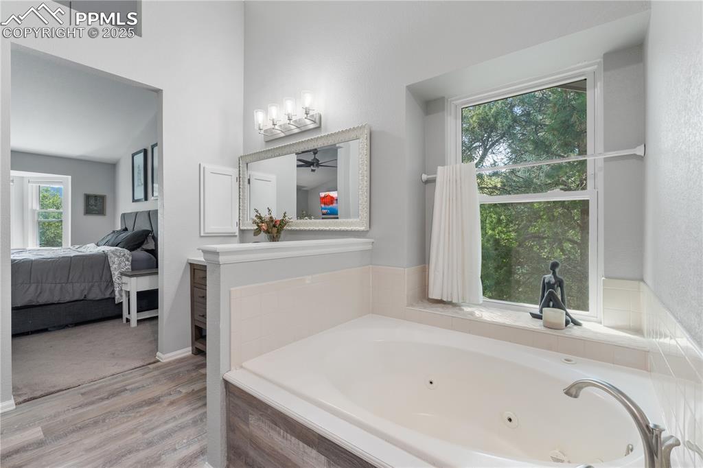 Image 26 of 50: Full bath featuring connected bathroom, a tub with jets, wood finished floo