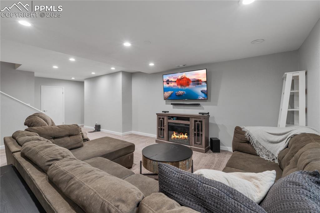 Image 36 of 50: Living room with recessed lighting, a glass covered fireplace, and stairs