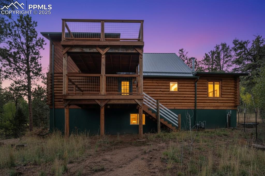 Image 3 of 48: Back of property at dusk featuring stairway, a wooden deck, log siding, and