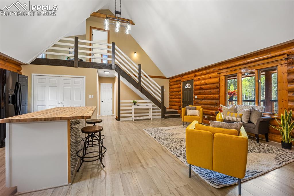 Image 7 of 48: Living room with high vaulted ceiling, light wood-style floors, rustic wall