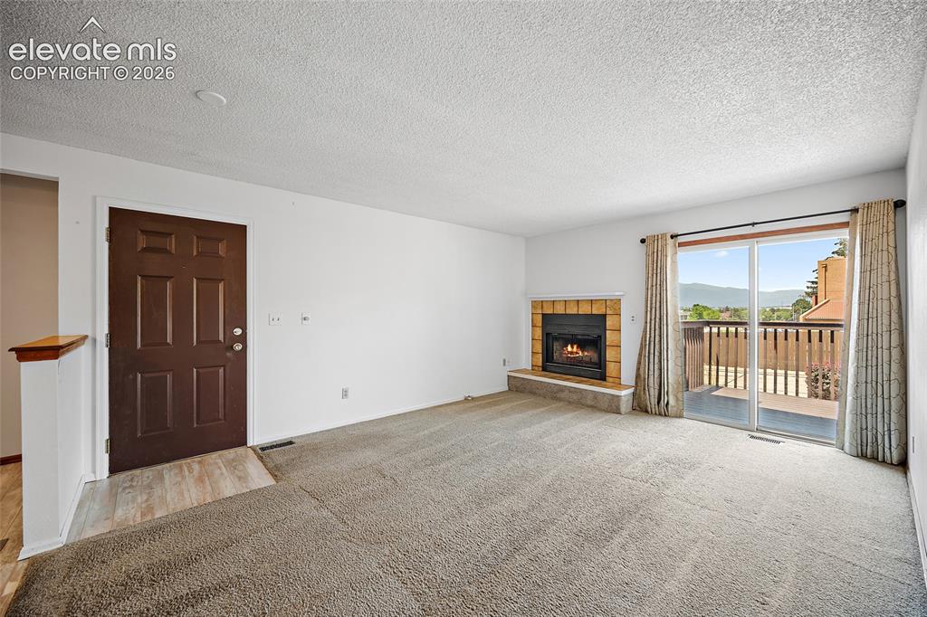 Image 17 of 26: Spacious living area featuring a fireplace with a tile surround, carpeted f