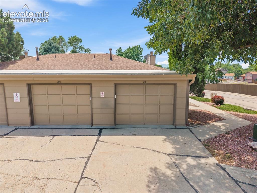 Image 21 of 26: Two single-car garages with panel-style doors and a brown shingled roofline