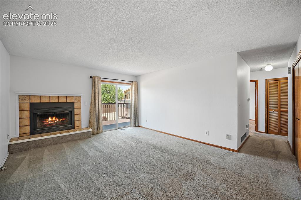 Image 4 of 26: Living area featuring a tiled fireplace, light-toned carpeting, and white w