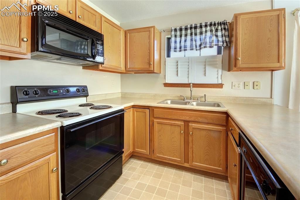 Image 10 of 33: Kitchen with electric stove, black microwave, light countertops, and brown