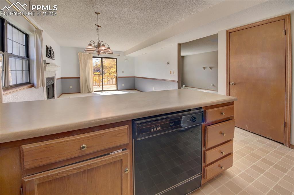 Image 11 of 33: Kitchen featuring black dishwasher, a fireplace, a textured ceiling, light