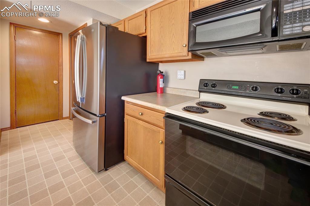 Image 12 of 33: Kitchen with black appliances, light countertops, light brown cabinetry, re