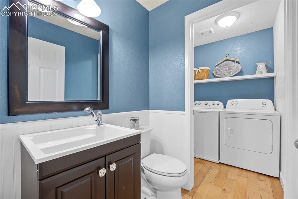 Image 22 of 50: Bathroom with light wood-style floors, vanity, washer and dryer, wainscotin
