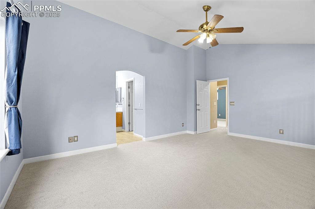 Image 28 of 50: Empty room with light carpet, high vaulted ceiling, arched walkways, and ce