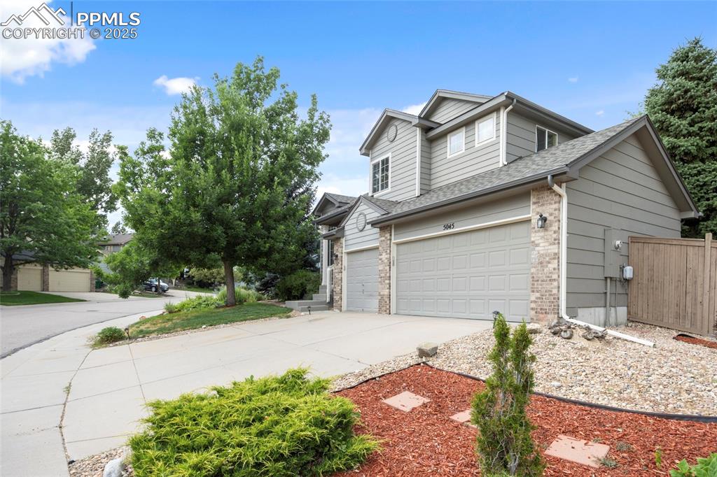 Image 4 of 50: View of side of home with driveway, brick siding, an attached garage, and a