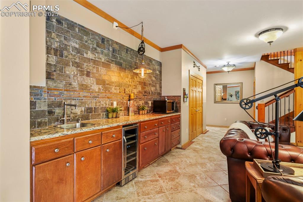 Image 34 of 50: Wet at area in basement living room with wine cooler, cabinets, and backspl