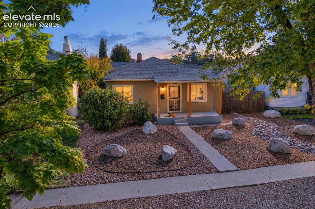 Caption: Stucco exterior with a covered front porch, a gabled roof, and a concrete walkway