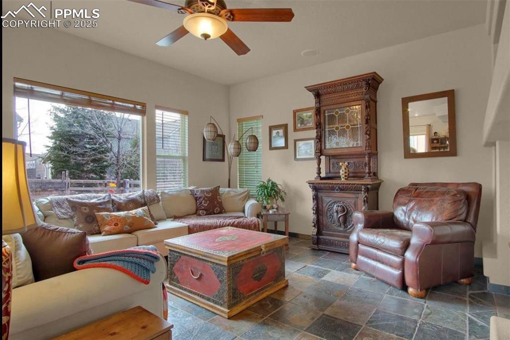 Image 14 of 42: Living room with stone tile flooring, a ceiling fan, and baseboards