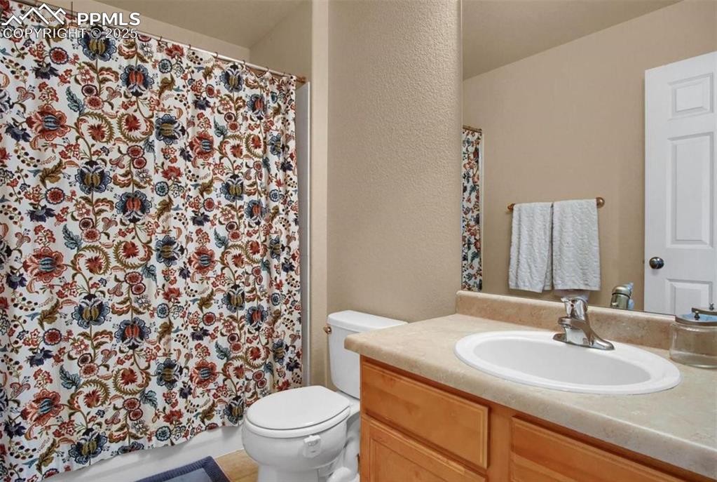 Image 21 of 42: Full bath with vanity, a textured wall, a shower with shower curtain, and t