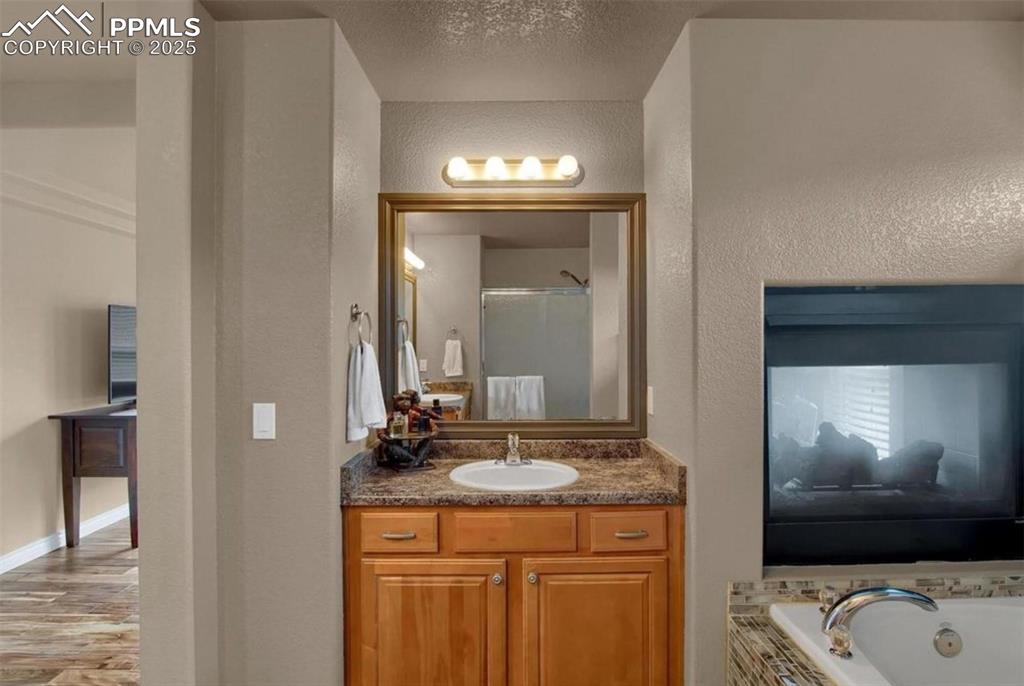 Image 26 of 42: Bathroom featuring a textured wall, a tub with jets, wood finished floors,