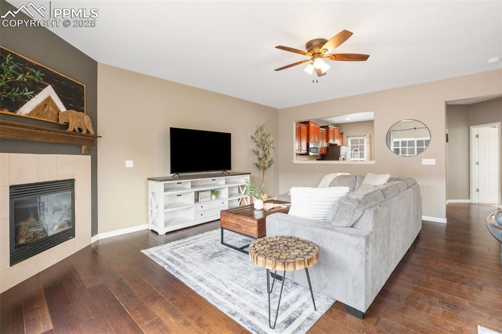 Image 6 of 35: Living area with a ceiling fan, a tile fireplace, and dark wood finished fl