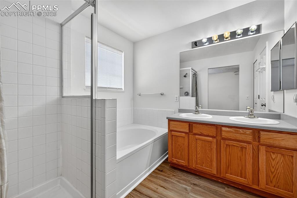 Image 19 of 29: Bathroom featuring double vanity, a bath, a stall shower, and light wood-st