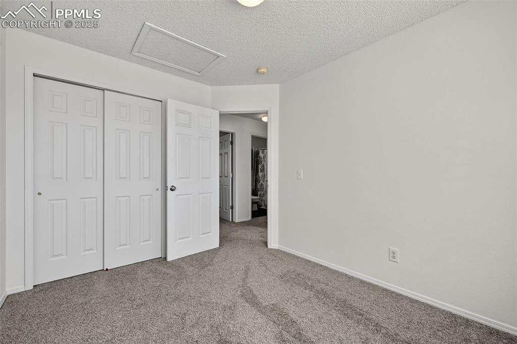 Image 21 of 29: Unfurnished bedroom featuring attic access, carpet floors, a textured ceili