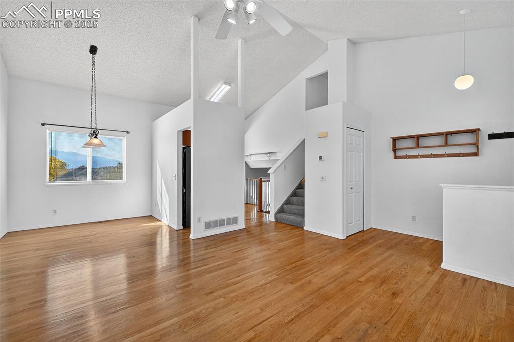 Image 8 of 29: Living room with light wood finished floors, high vaulted ceiling, stairs, 