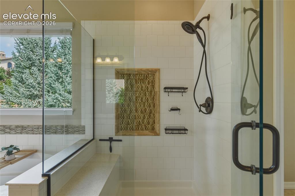 Image 21 of 49: Glass-enclosed shower with a built-in bench, white subway tile surround, an