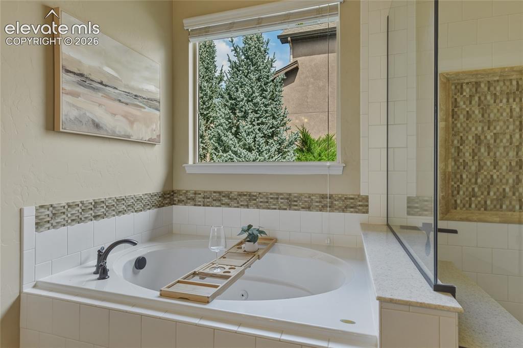 Image 22 of 49: Built-in soaking tub with a tiled surround, mosaic accent trim, and a matte