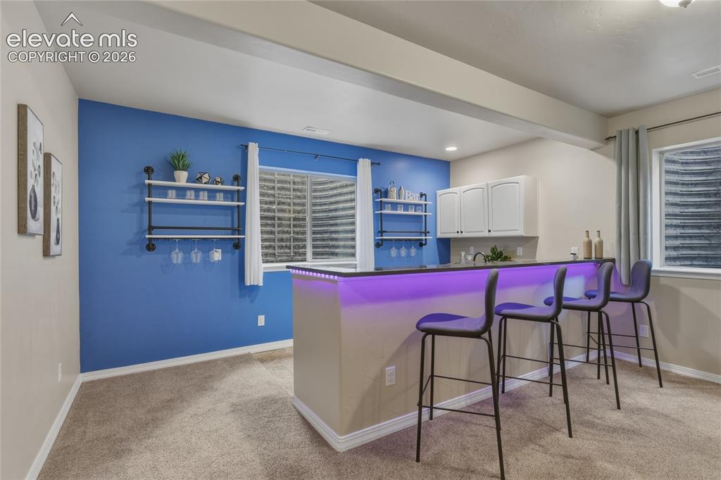 Image 29 of 49: Built-in wet bar with white cabinetry, dark countertop, and custom lighting
