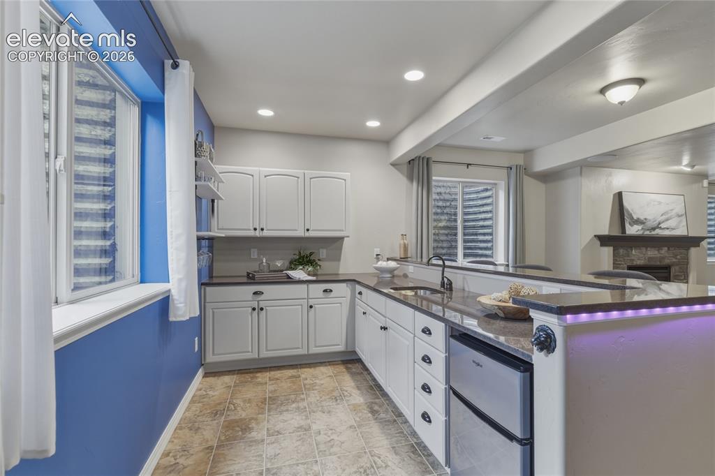Image 30 of 49: Kitchenette featuring white cabinetry, dark countertops, a built-in sink wi